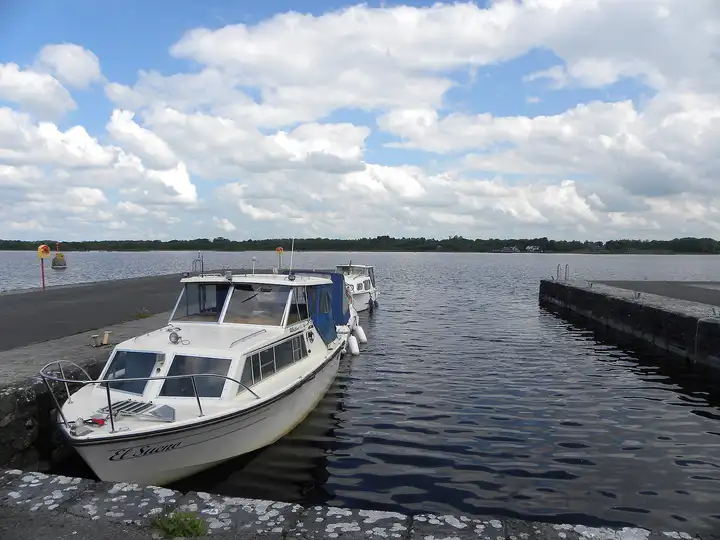 Two motor cruisers moored inside the stone harbour at Knockferry Pier, looking out across the narrows of Lough Corrib to the wooded far shore.