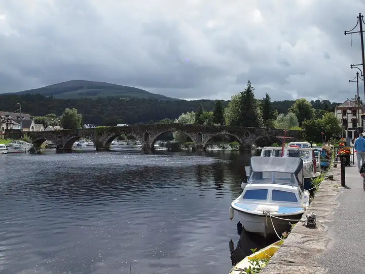 Cruisers moored at the quay in Graiguenamanagh beside the many-arched stone bridge, with Brandon Hill rising beyond.