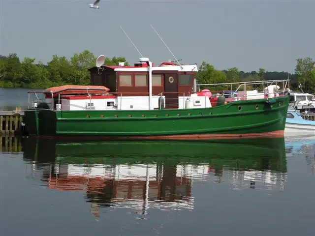 Een motorschip met groene romp en wit-bruine kajuit ligt in de kalme jachthaven van Ballyronan en spiegelt in het water.