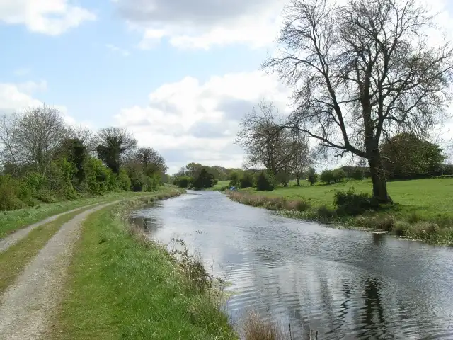 Bei Thomastown schwingt sich der Kanal sanft zwischen grasigem Treidelpfad und Feldern unter frühlingshaften Bäumen dahin, seine Oberfläche kräuselt sich unter einem wolkengetupften Himmel.