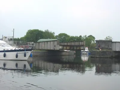 The swing span of Portumna Bridge turned open for boats, with a cruiser in the foreground and a small boat waiting beyond.