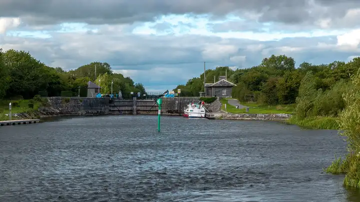 Victoria Lock seen from the river, with its closed gates, a green channel marker, a cruiser tied up at the approach wall and the lock house among the trees.