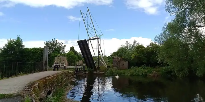The raised lifting bridge at Bagenalstown Lock, its steel frame above the lock entrance, with a swan on the calm river.