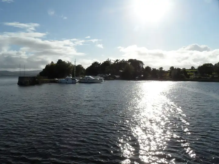 Williamstown harbour seen from the lake against the afternoon sun, with cruisers moored behind the stone pier and trees along the Clare shore.