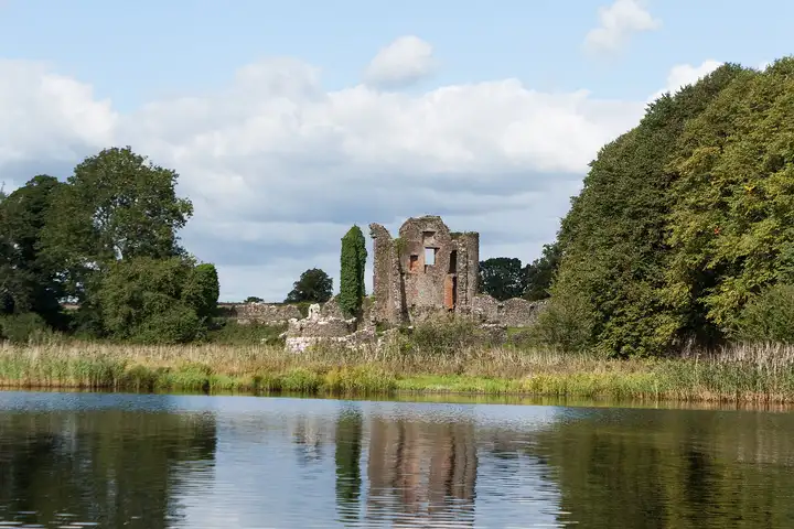 The ruins of Old Crom Castle stand among trees above a reedy shore, reflected in the calm water of Upper Lough Erne.