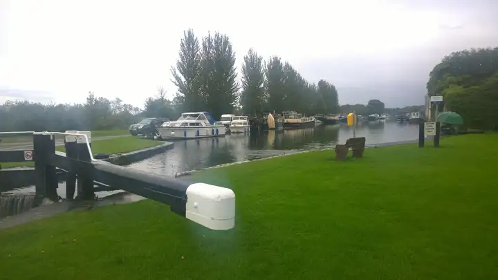 Op de voorgrond de zwart-witte balk van de 35e sluis, daarachter motorboten en aken in de kanaalhaven.