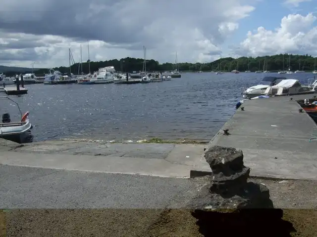 The slipway and concrete pier at Mountshannon, with motor boats in the harbour and yachts moored out in the bay under a cloudy sky.