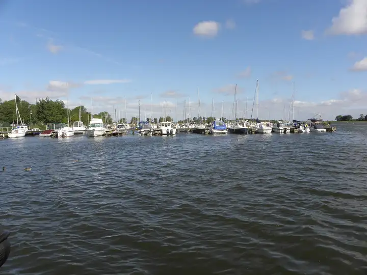 Eine lange Reihe von Segeljachten und Motorbooten in der Kinnego Marina, über bewegtes Wasser hinweg unter blauem Himmel mit kleinen Wolken.