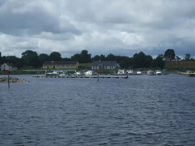 Le ponton flottant de Portrunny et ses bateaux amarrés, vus depuis le lac, avec des maisons et des arbres sur la rive derrière.