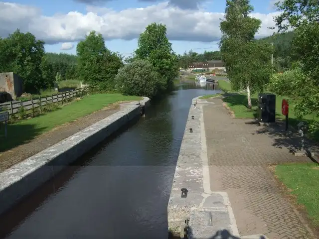 Looking along a lock chamber at Kilclare on a sunny day, with the paved lockside and control pillars on the right and moored boats and a red-roofed building in the distance.