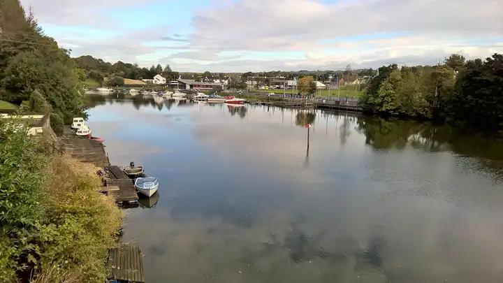 Small boats lie at the pontoons and wooden jetties of Portglenone’s marina on the calm River Bann, with village houses and trees reflected beyond.