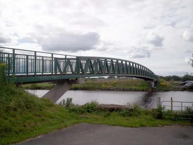 The Ferry cycle bridge, a curved green steel footbridge on a concrete pier, crosses the water near Maghery Country Park.