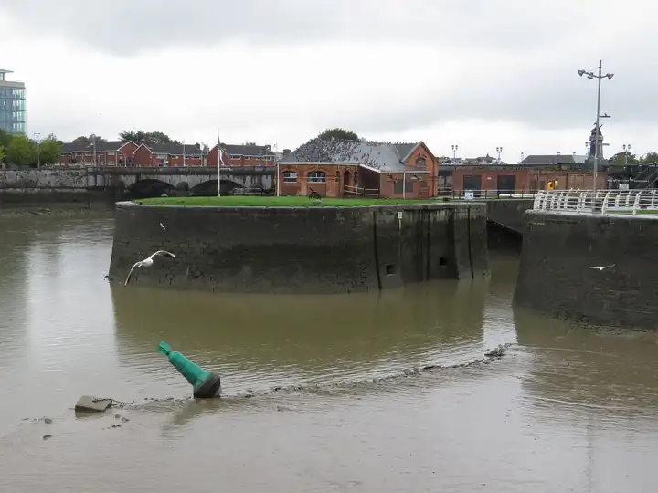 At low tide a green channel buoy lies on the mud before the stone pierheads at the seaward entrance to Sarsfield Lock.