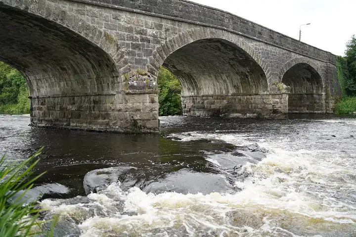 White water rushes over the rocks below the stone arches of the Erne Bridge in Belturbet.