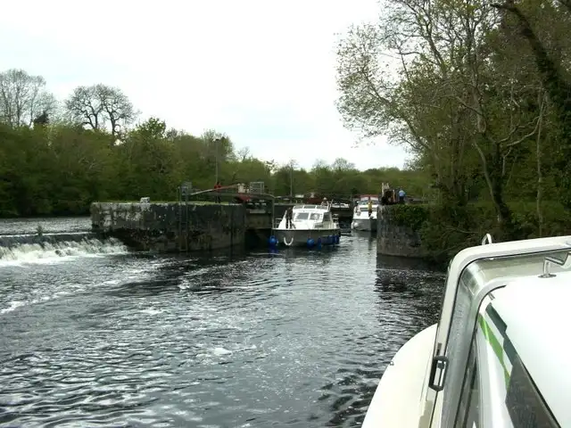 Seen from the bow of an approaching cruiser, Clarendon Lock lies ahead with a boat in the chamber and water spilling over the weir to the left.
