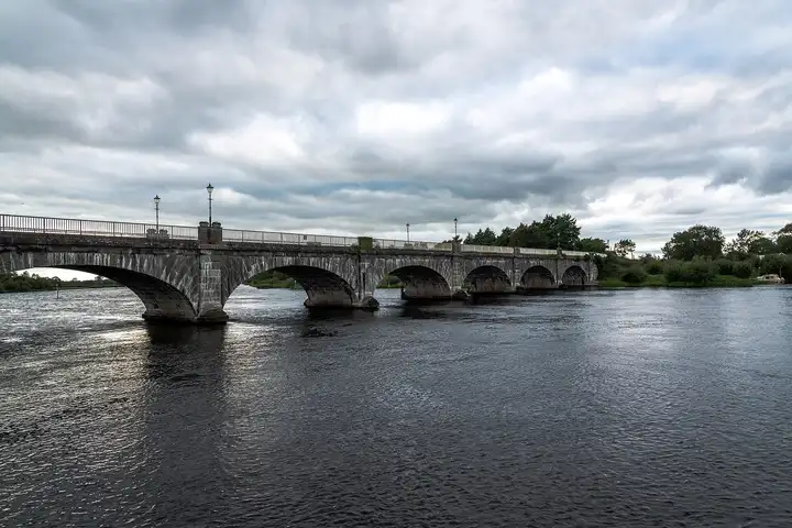 The masonry arches of Banagher Bridge stretch across the wide, rippled Shannon under a heavy, cloudy sky.