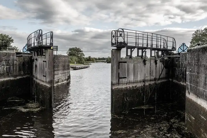 View out through the open gates of Victoria Lock, with railed walkways on top, along the cut towards a floating jetty under a cloudy sky.