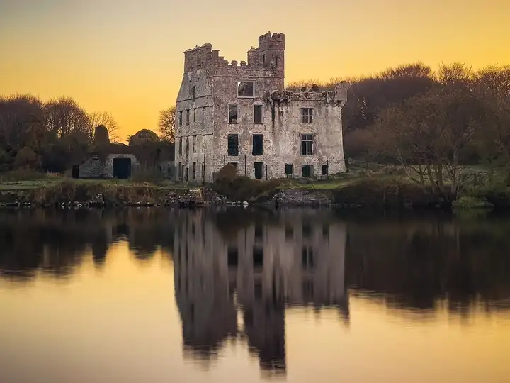 La ruine sans toit du château de Menlo se reflète dans les eaux calmes de la rivière Corrib à l’aube, sous un ciel doré.