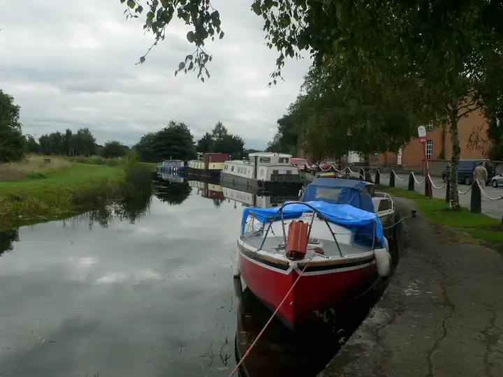 Boats moored along the stone quay at Robertstown, with a red-and-white cruiser in the foreground and barges further along under the trees.