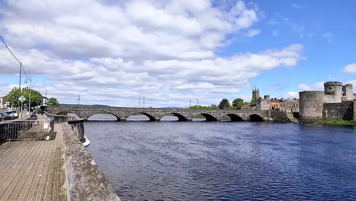 Von einem hölzernen Uferweg geht der Blick über den Shannon zu den Bögen der Thomond Bridge und den Rundtürmen von King John’s Castle.