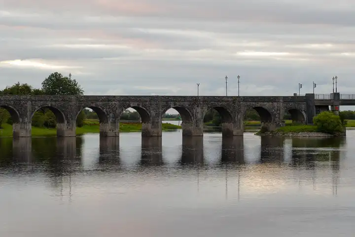 The stone arches of the bridge at Shannonbridge reflected in the still Shannon under a pink-tinged evening sky.