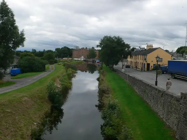 Le canal à Robertstown vu depuis un pont, filant vers le grand bâtiment en brique du Grand Canal Hotel, avec une rangée de maisons jaunes le long de la route à droite.