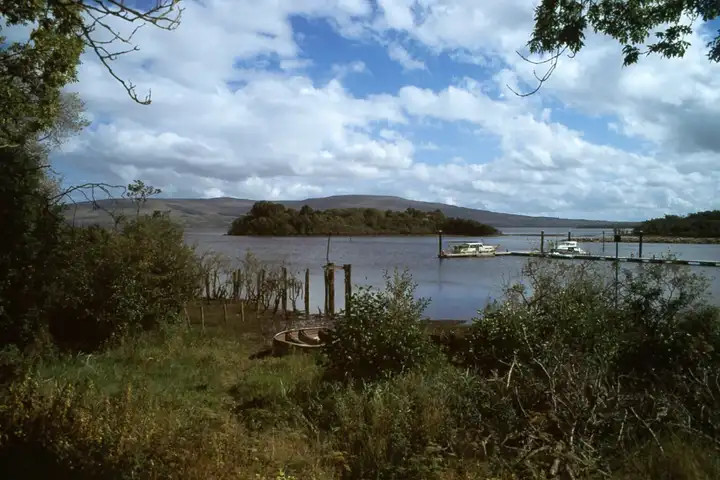 Two cruisers lie at the jetty of Spencer Harbour on Lough Allen, with wooded Corry Island and the hills beyond under white clouds.