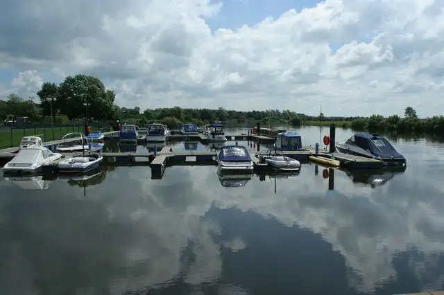 Motor cruisers moored at the pontoons of Drumaheglis Marina, mirrored with white clouds in the still water of the Bann.