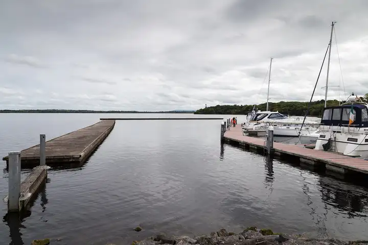 The floating jetties of Garrykennedy marina under a grey sky, with yachts moored on the right and Lough Derg beyond.