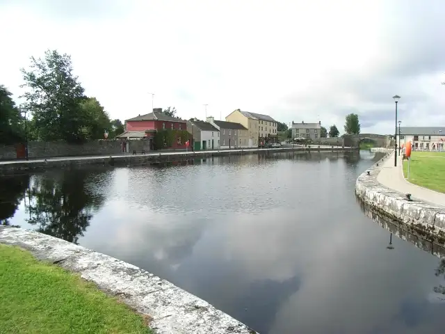 Le long bassin de pierre de Richmond Harbour, à Clondra, reflète un ciel pâle, avec les maisons peintes et les vieux bâtiments du village le long du quai opposé.