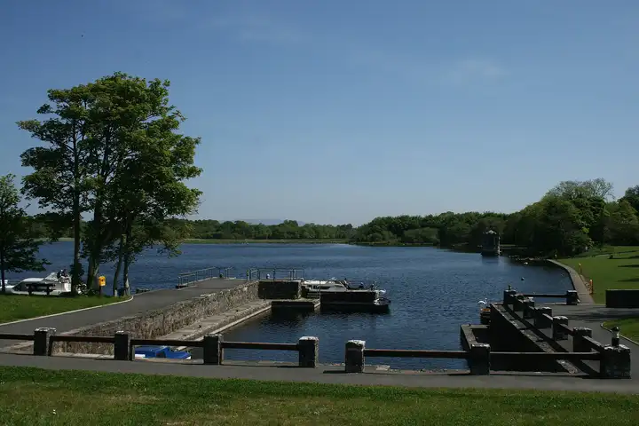 The stone harbour at Lough Key Forest Park on a sunny day, with a cruiser at the jetty, swans on the water and the lake stretching away under a blue sky.