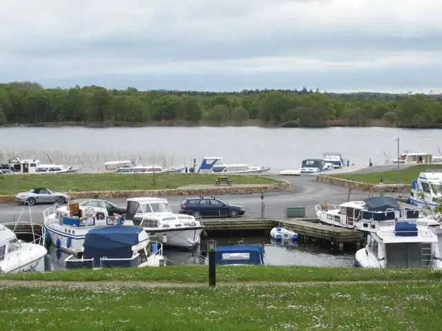 Motorboote liegen in einem Marinabecken am Ostende des Lough Key bei Knockvicar, auf dem Kai parken Autos, gegenüber bewaldete Ufer.