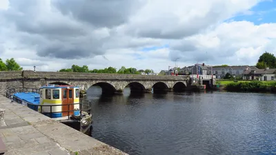 Roosky’s long stone bridge crosses the Shannon on a row of arches, with a blue-and-cream boat moored at the quay in the foreground and the lifting span on the far right.