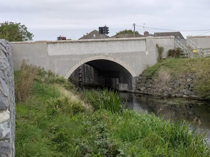 De gepleisterde boog van de verkeersbrug bij de 12e sluis, met hoog gras en riet op de kanaaloever ervoor.