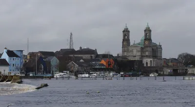The Shannon at Athlone, with the weir in the foreground, boats moored along the far quay and the twin towers and dome of the Church of Saints Peter and Paul above the town.