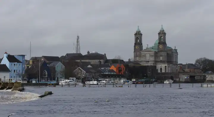 The Shannon at Athlone, with the weir in the foreground, boats moored along the far quay and the twin towers and dome of the Church of Saints Peter and Paul above the town.