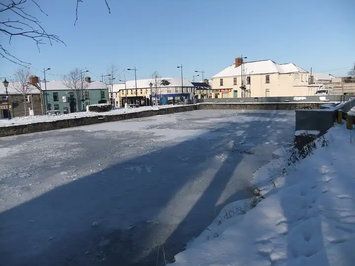 Le port d’Edenderry gelé et saupoudré de neige par une journée d’hiver ensoleillée, avec les maisons et commerces de la ville le long du quai.