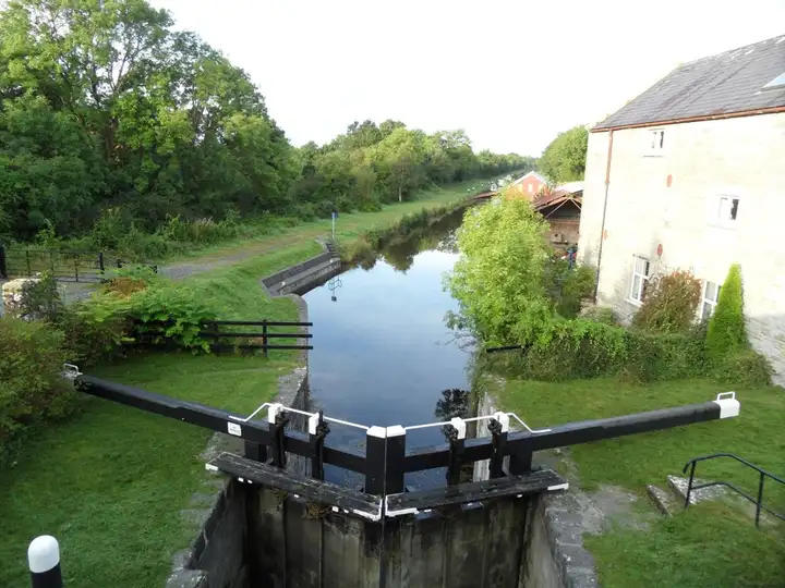 Looking down from the 33rd Lock at Belmont over its closed wooden gates, with the canal stretching away between a towpath and an old stone house.