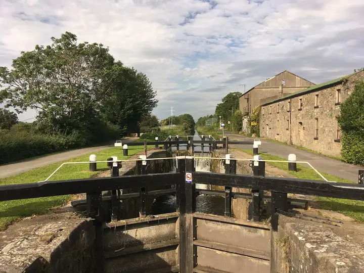 The 12th Lock seen over its wooden gates, with white-capped bollards along the chamber, the canal continuing beyond and a long old stone building on the right.