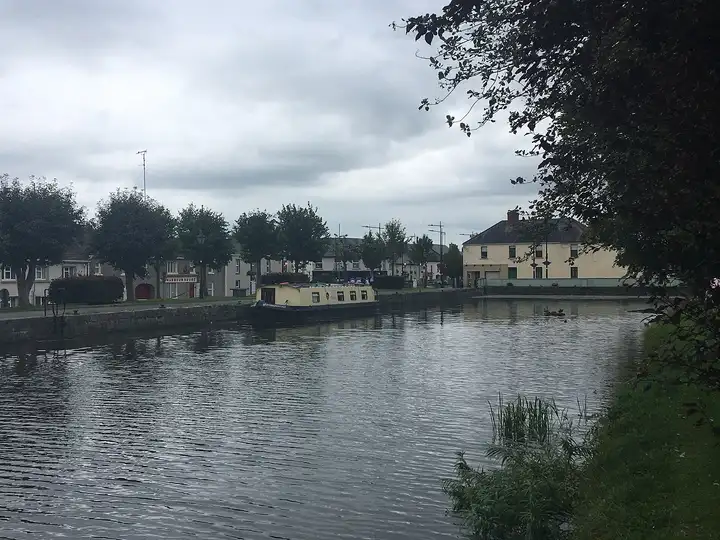Edenderry Harbour under a grey sky, with a cream narrowboat moored at the stone quay and the town’s houses, including Harbour House, along the far side.