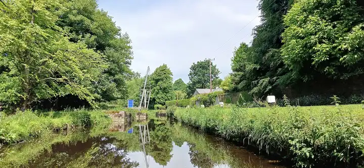 La dérivation bordée d’arbres près de l’écluse d’Ardreigh, avec le pont levant de Coneyburrow relevé, reflété dans l’eau calme.