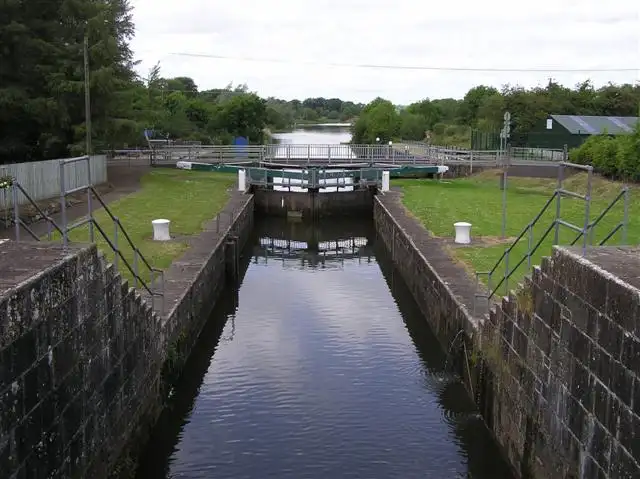 Looking along the stone-walled chambers of the double lock at Portna, past white bollards and closed gates towards the river beyond.