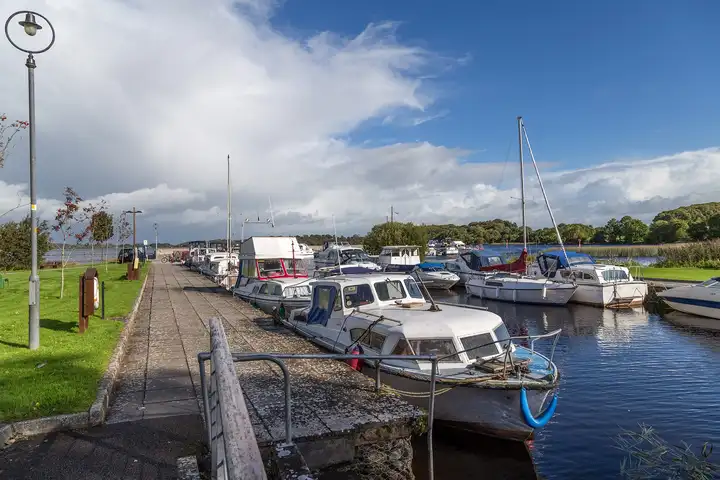 Cruisers and sailing boats moored along the paved quay of Terryglass inner harbour under a dramatic blue and white sky.
