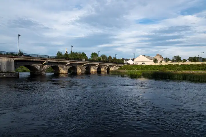 De Shannon bij Lanesborough op een zomeravond, met de lange boogbrug en witte huizen op de met riet begroeide oever.