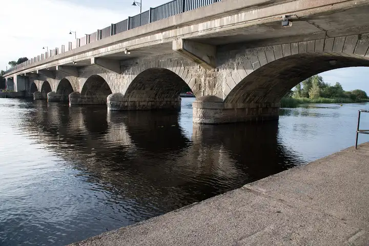 Nahaufnahme der steinverkleideten Bögen und Pfeiler der Brücke von Lanesborough vom Kai aus, darunter fließt der dunkle Fluss.