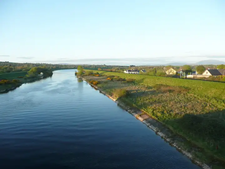 The headrace canal stretches into the distance at Clonlara in low sunlight, with houses along the embankment on the right.