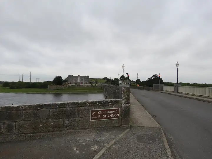 Sur le tablier du pont de Shannonbridge, avec un panneau brun indiquant le Shannon sur le parapet de pierre et le vieux fort au bout de la route.