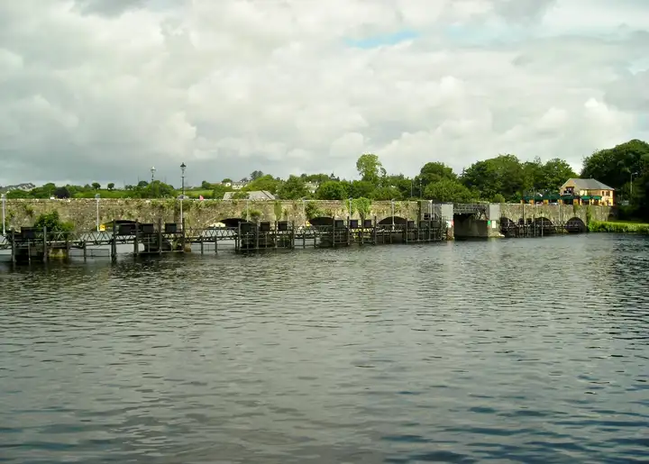 Le long pont bas à arches entre Killaloe et Ballina vu depuis la rivière, avec une rangée de structures métalliques de barrage devant ses arches.