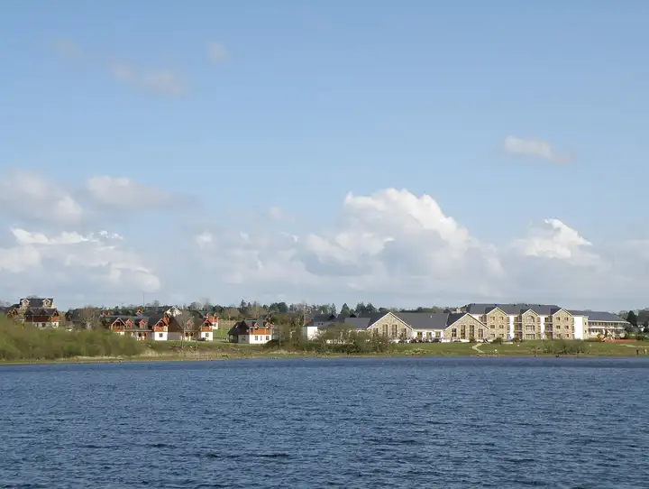 Holiday homes and a large stone-fronted building line the shore at Drumshanbo, seen across the open water of Lough Allen under a blue sky.