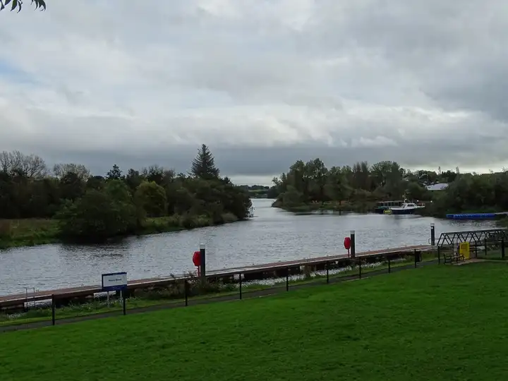 Ein langer Steg mit roten Rettungsringen zieht sich unter grauem Herbsthimmel an einer Rasenböschung des River Erne in Enniskillen entlang.